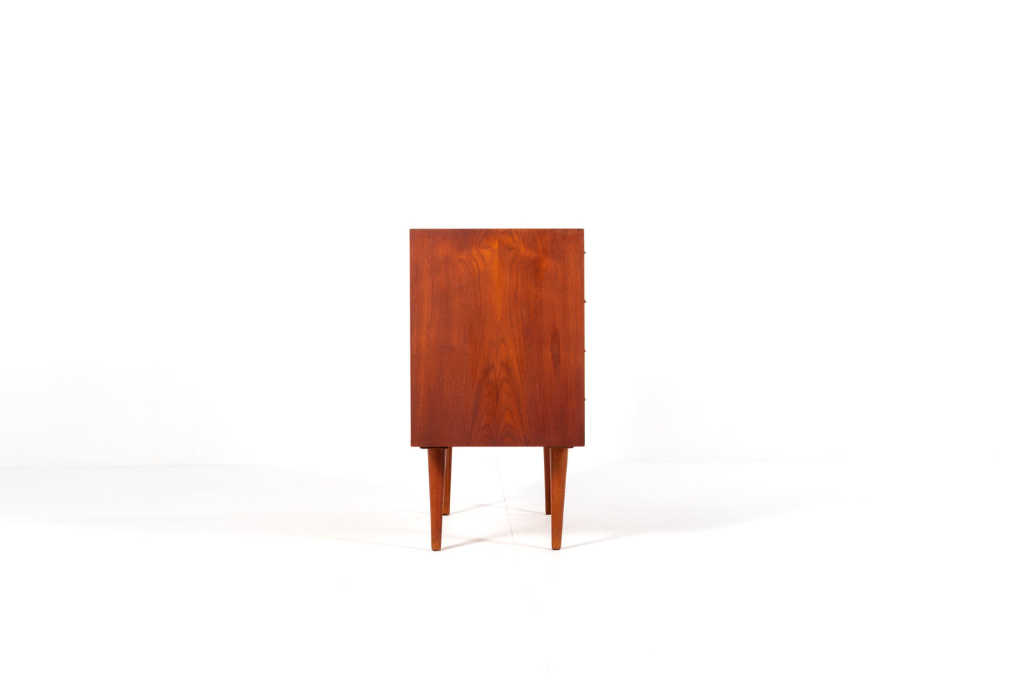 A mid-century modern wooden chest of drawers with five drawers by Kai Kristiansen, shown against a plain white studio background., side view