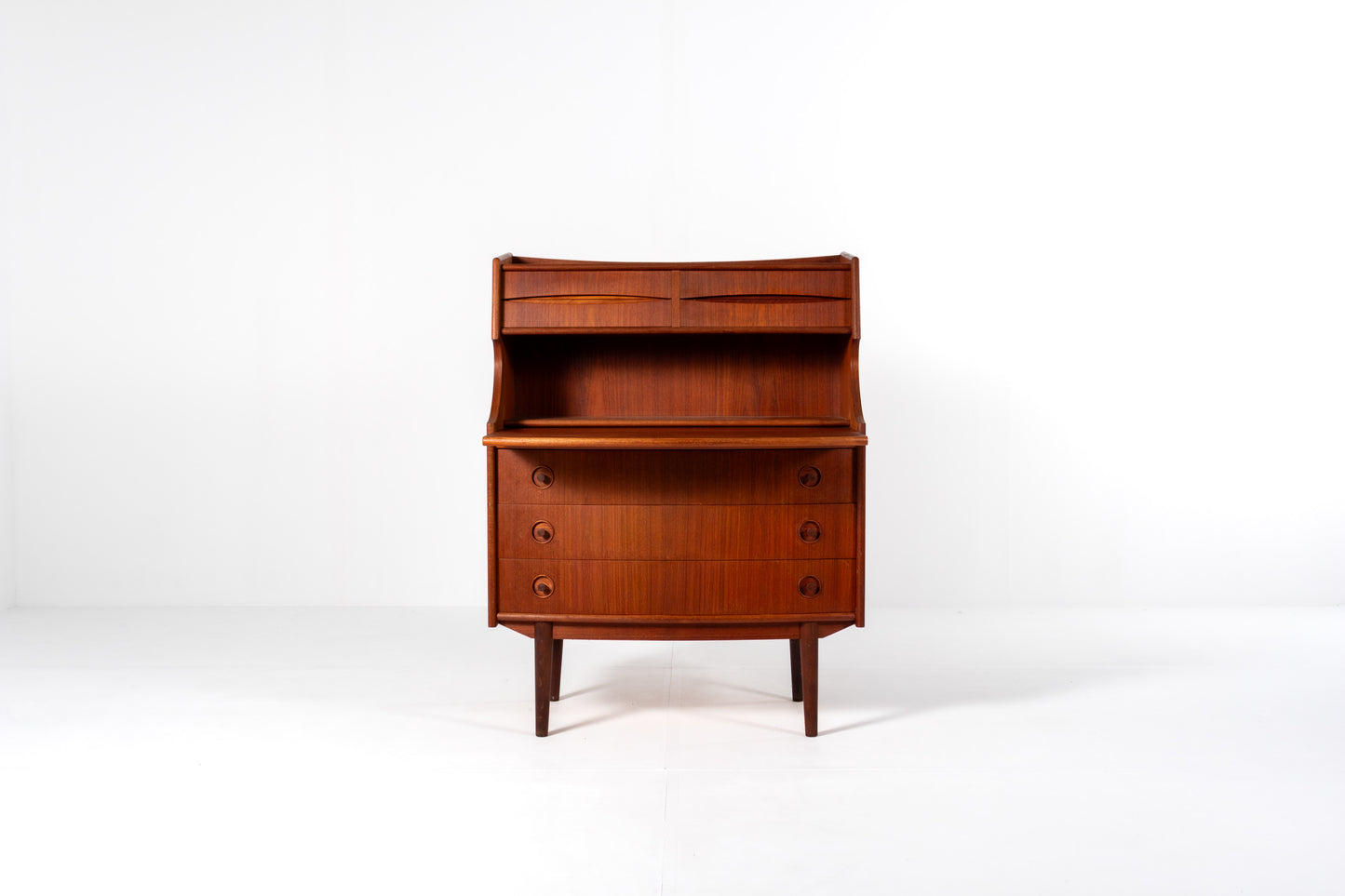 A mid-century modern wooden writing desk by Gunnar Falsig for Falsig Møbler with a warm reddish-brown finish, featuring a curved top, open shelf, and three drawers on the lower cabinet, set against a plain white studio background.