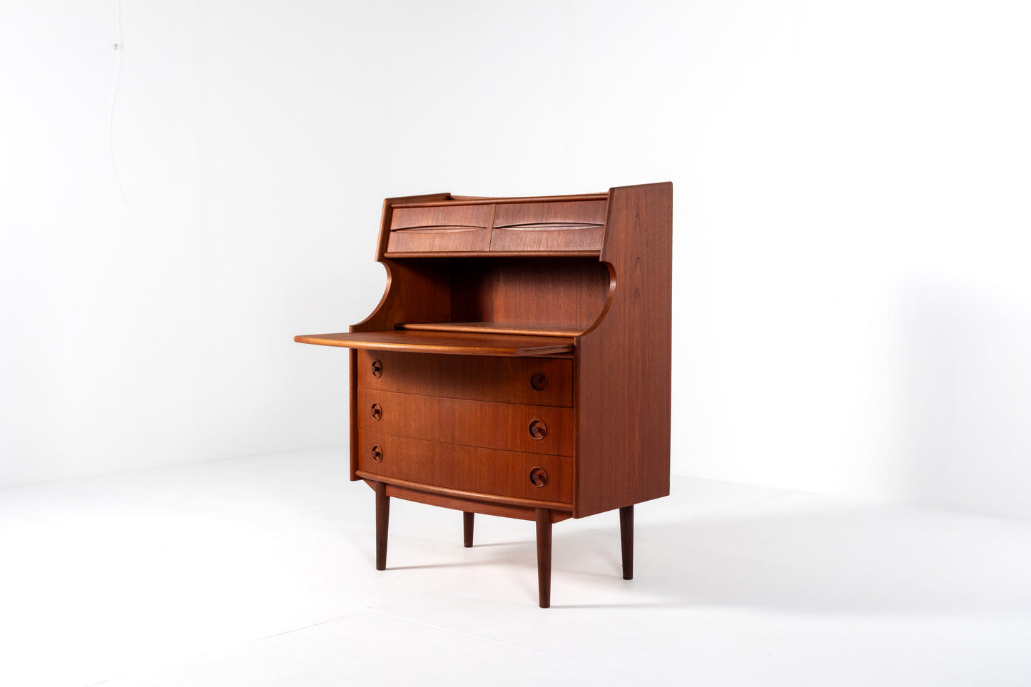 A mid-century modern wooden roll-top desk with a warm reddish-brown finish, featuring three drawers with round knobs and tapered legs, photographed against a plain white studio background.