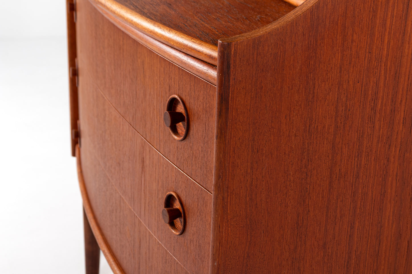 Close-up of a mid-century modern wooden side table or cabinet with two drawers, featuring a curved front, rich reddish-brown wood grain, and matching round drawer pulls.