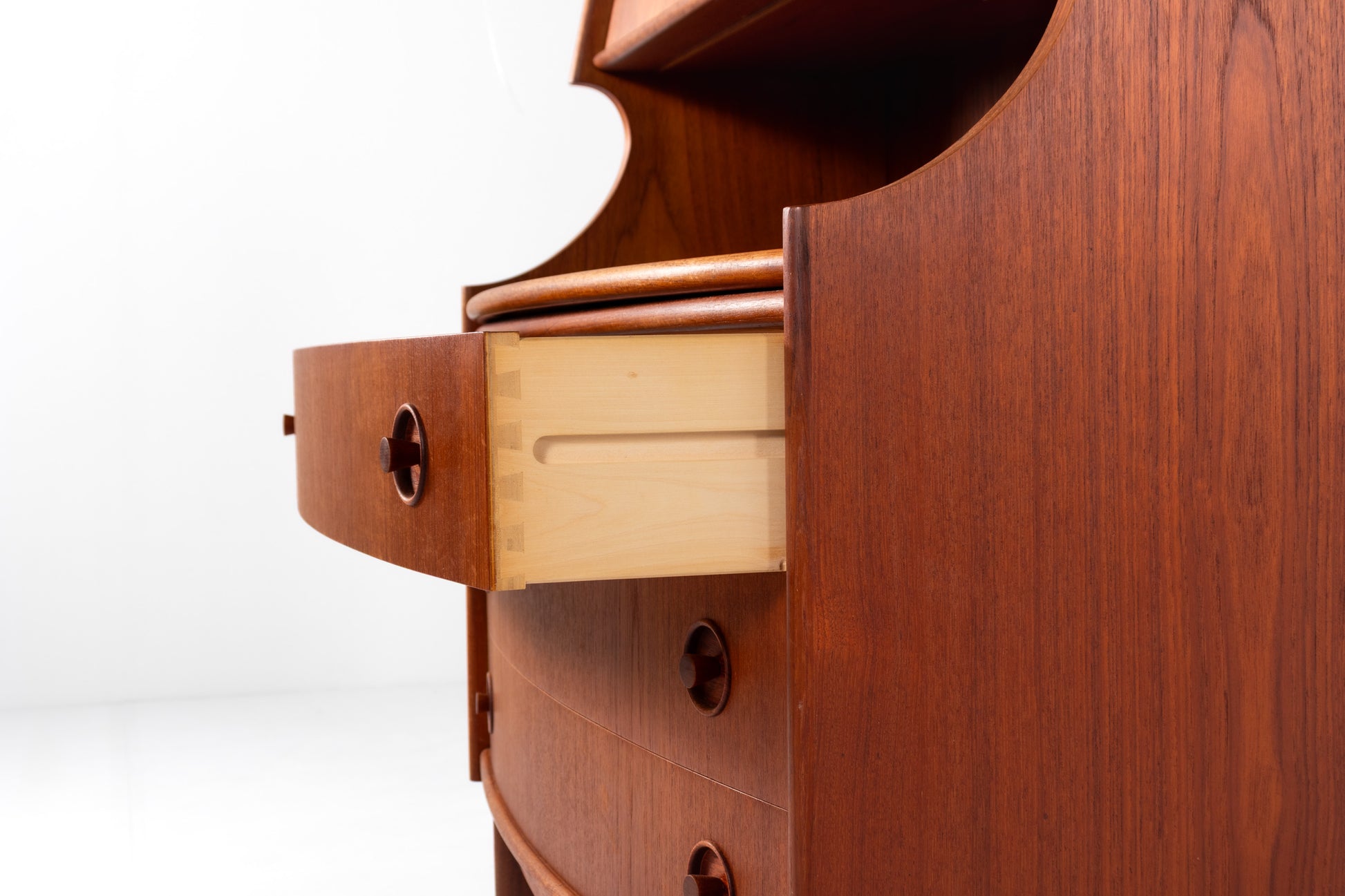Close-up of a mid-century modern wooden writing desk with a warm reddish-brown finish and a light natural wood drawer pull, set against a plain white background.