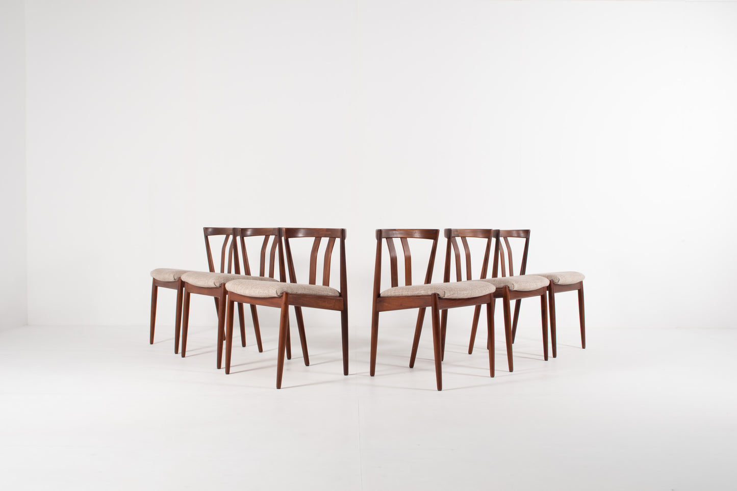 Six mid-century modern dining chairs  by Kai Kristiansen with dark brown teak frames and light grey upholstered seats, arranged in two pairs on a white studio background.