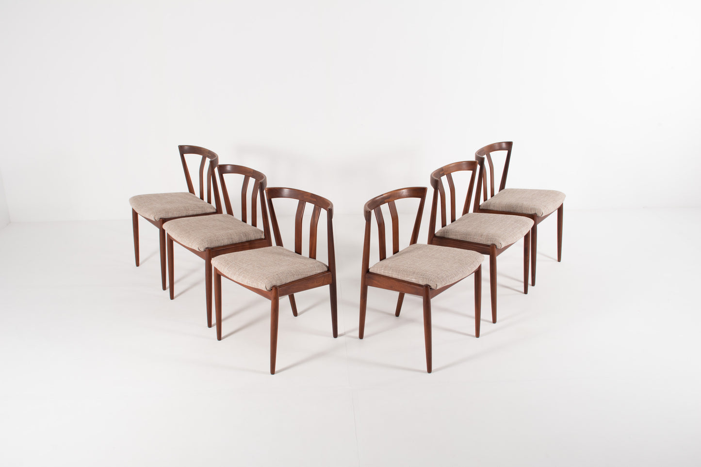 Six wooden dining chairs with curved backrests and light grey upholstered seats, arranged in two rows on a white studio background.