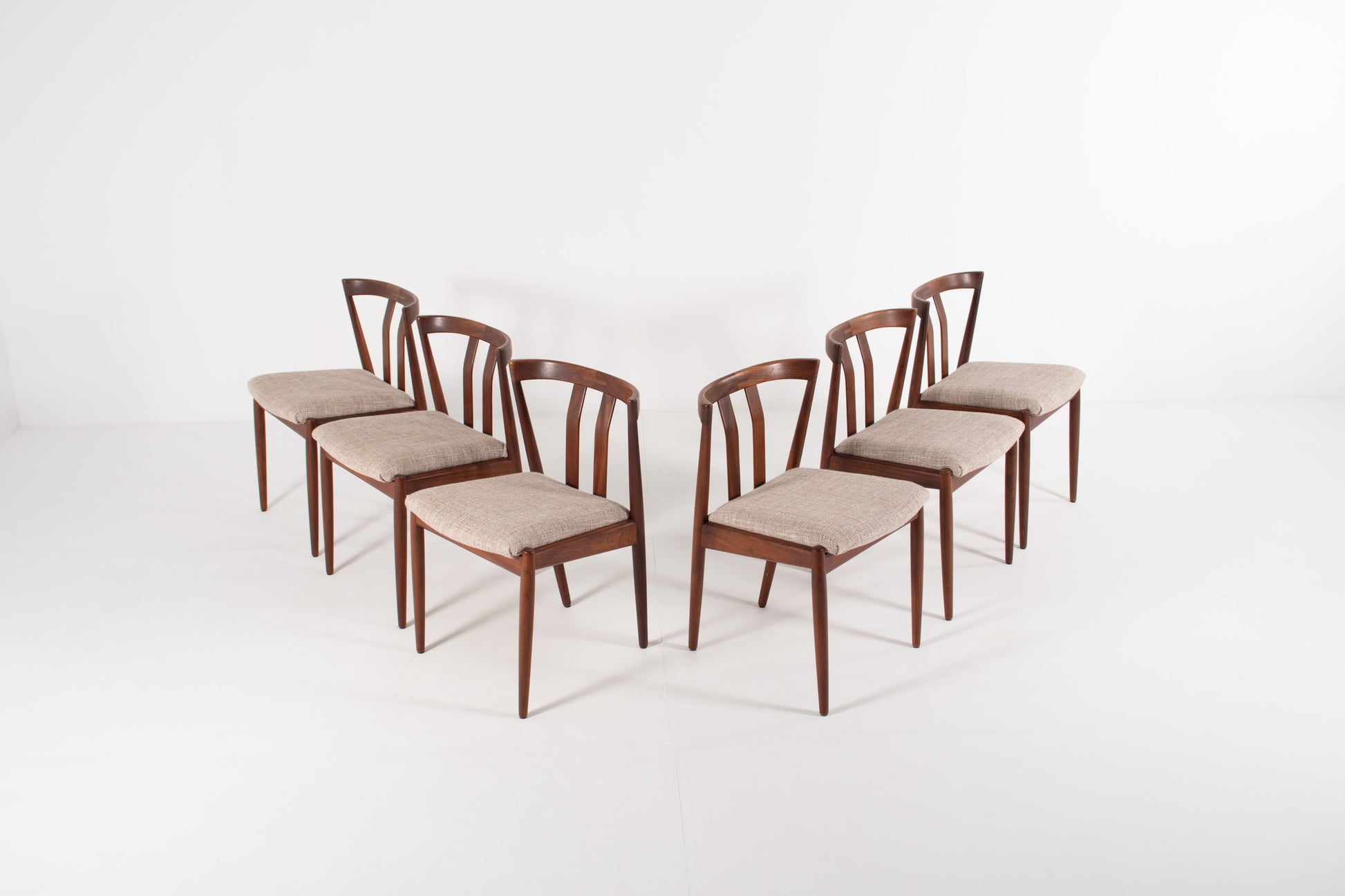 Six wooden dining chairs with curved backrests and light grey upholstered seats, arranged in two rows on a white studio background.