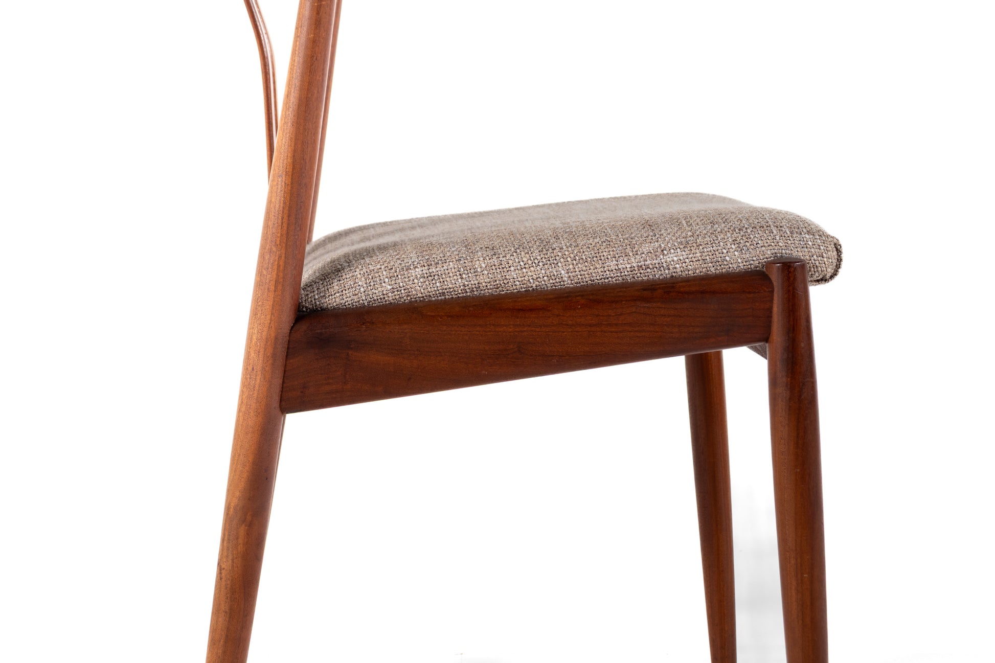 A close-up side view of a mid-century modern wooden dining chair with a textured taupe fabric seat cushion, set against a plain white background.