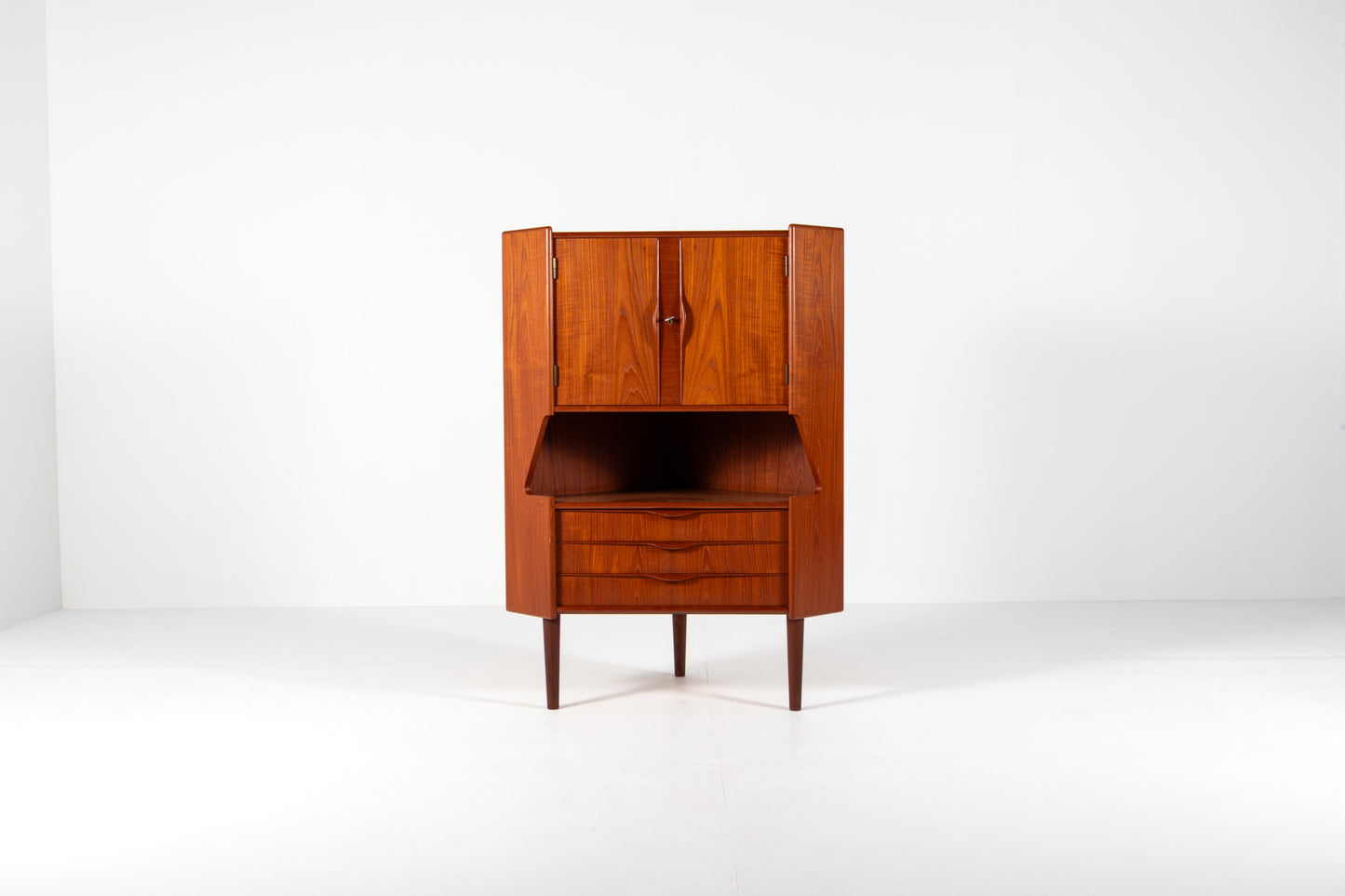 A mid-century modern wooden cabinet with a warm reddish-brown finish, featuring a closed upper cabinet, an open middle section, and two drawers below, set against a plain white studio background.