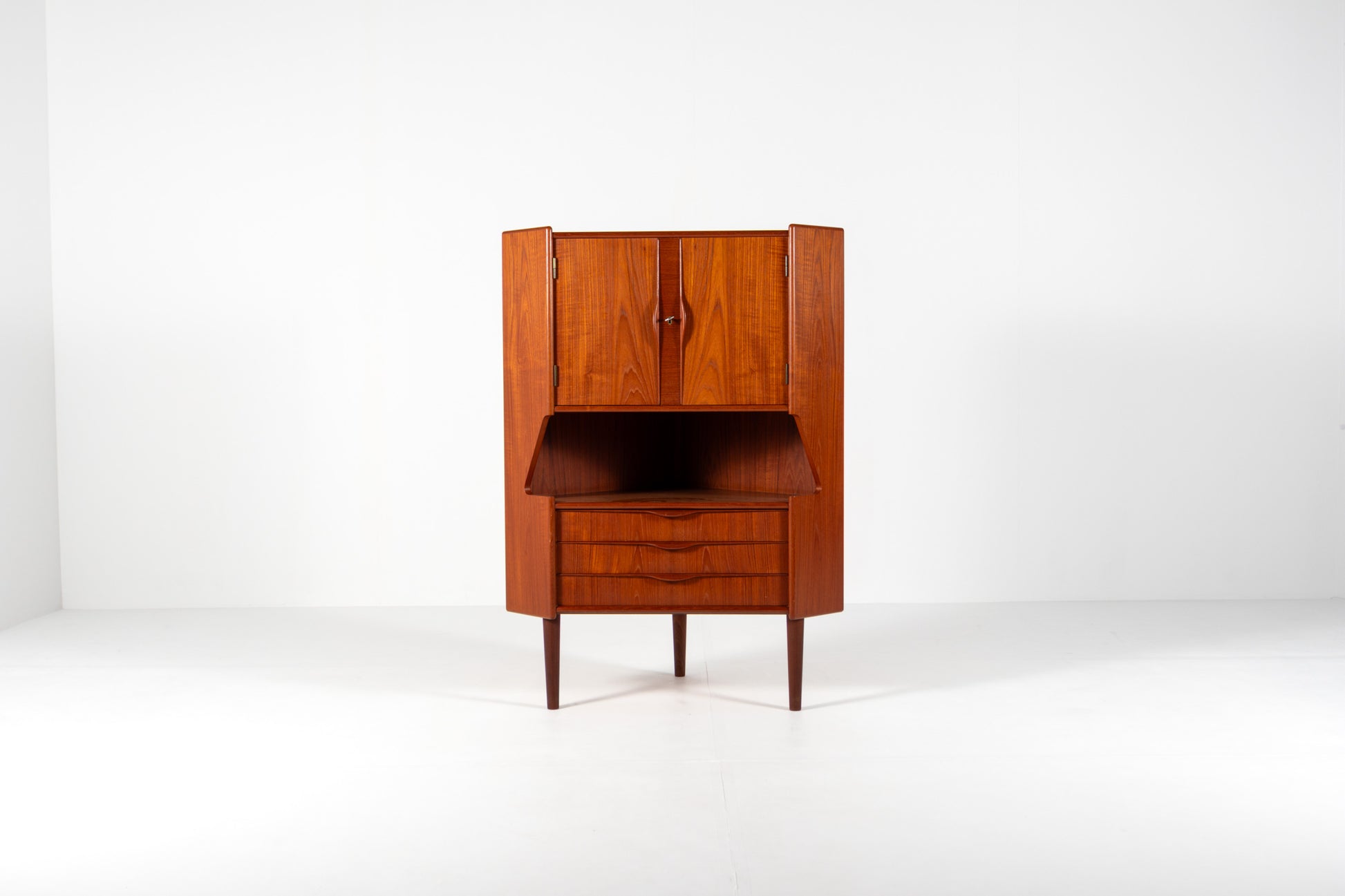 A mid-century modern wooden cabinet with a warm reddish-brown finish, featuring a closed upper cabinet, an open middle section, and two drawers below, set against a plain white studio background.