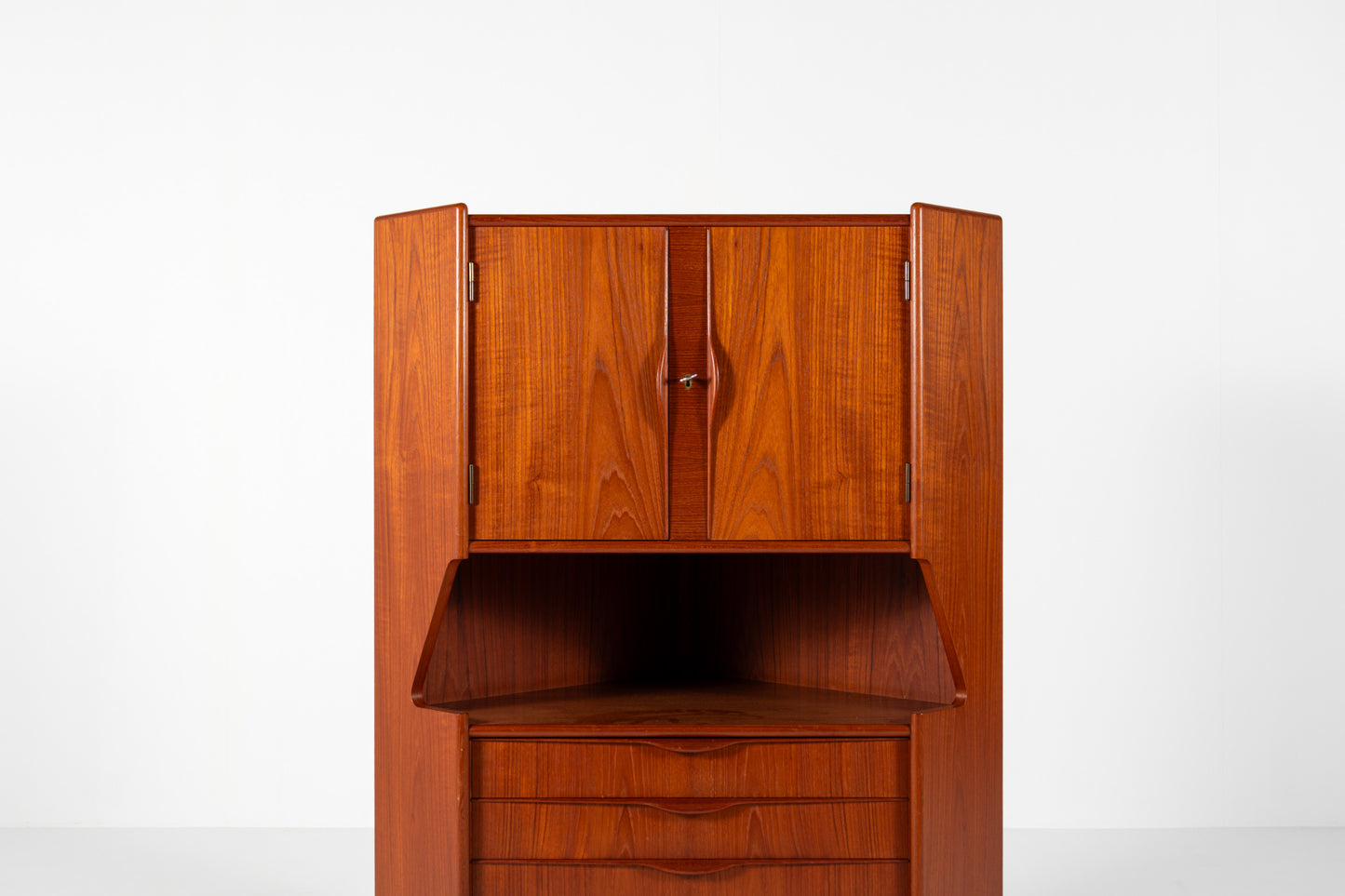 A mid-century modern wooden cabinet with a warm reddish-brown finish, featuring two upper doors, an open shelf, and three lower drawers, set against a plain white background.