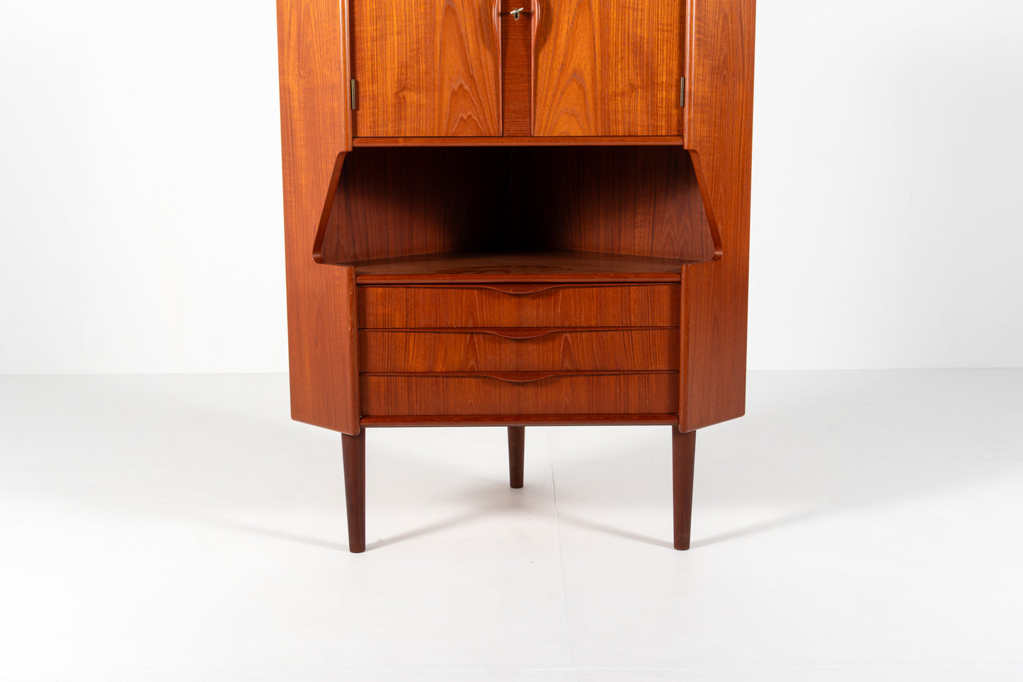 Mid-century modern wooden cabinet with a reddish-brown teak wood grain finish, featuring a lower section with three drawers and a hinged upper cabinet door open to reveal an interior shelf.