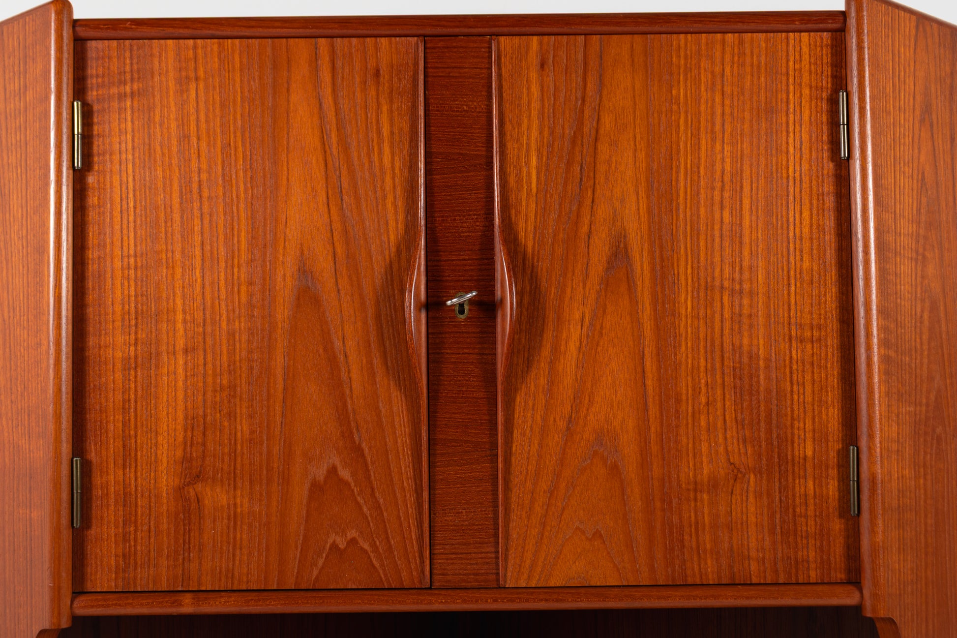 A close-up of a mid-century modern wooden cabinet with two doors, featuring a warm reddish-brown wood grain finish and small brass hinges.