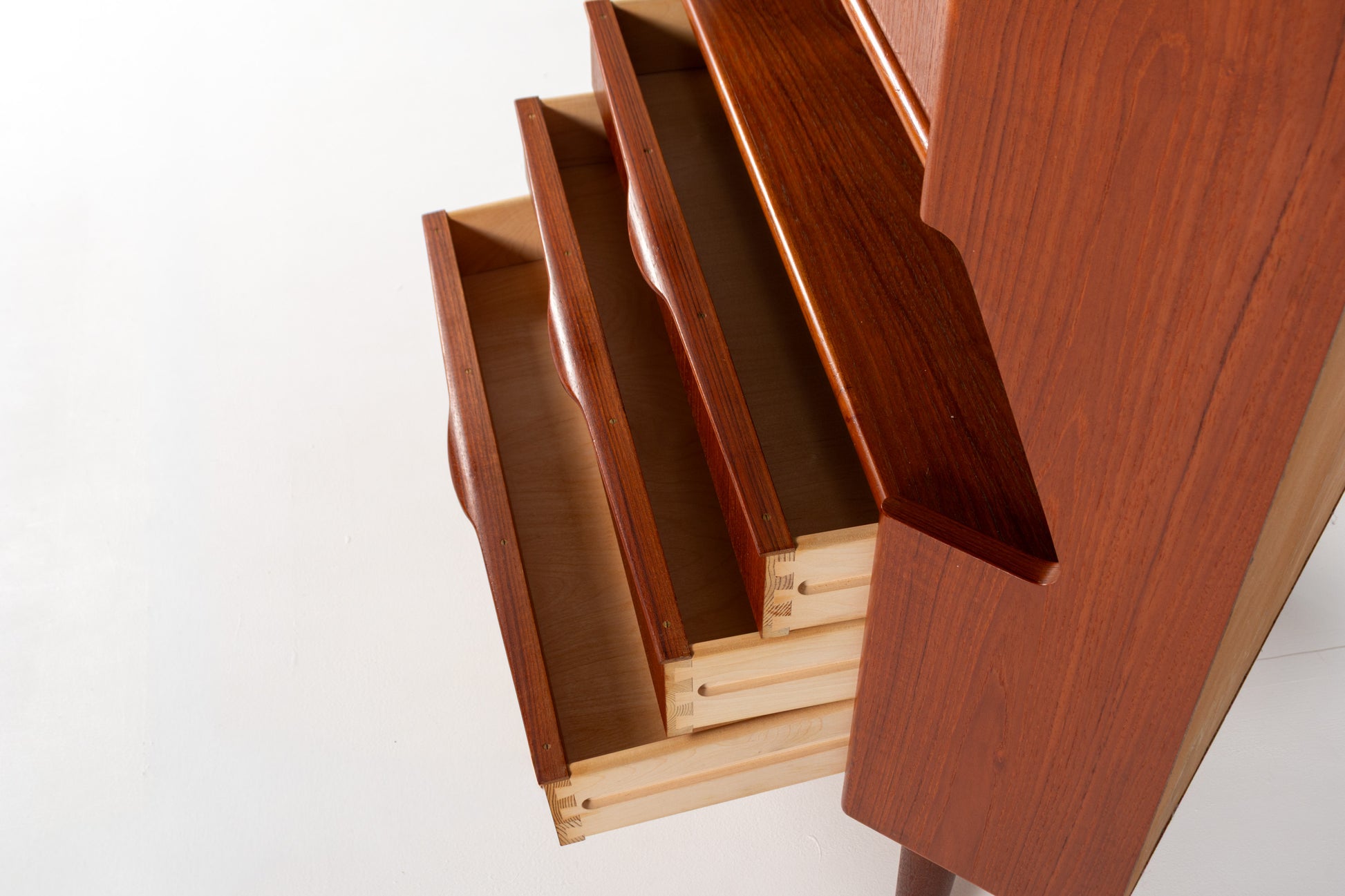 Close-up of a wooden cabinet or dresser with multiple drawers pulled open, showing the warm reddish-brown wood grain and light natural wood interiors against a plain white background.