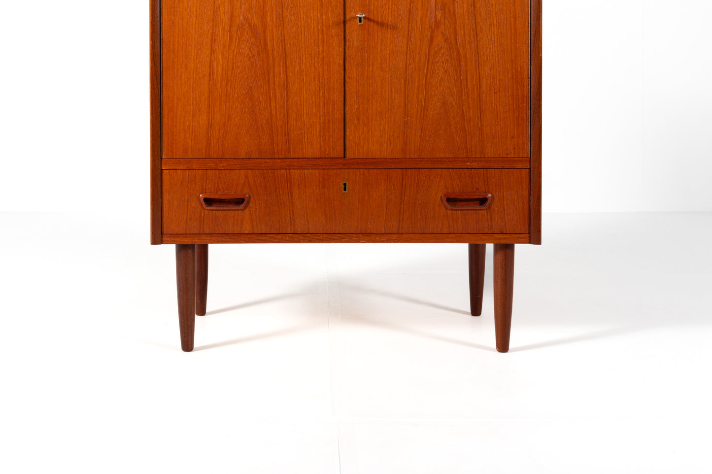A mid-century modern wooden cabinet with a warm reddish-brown finish, featuring two upper doors and a lower drawer