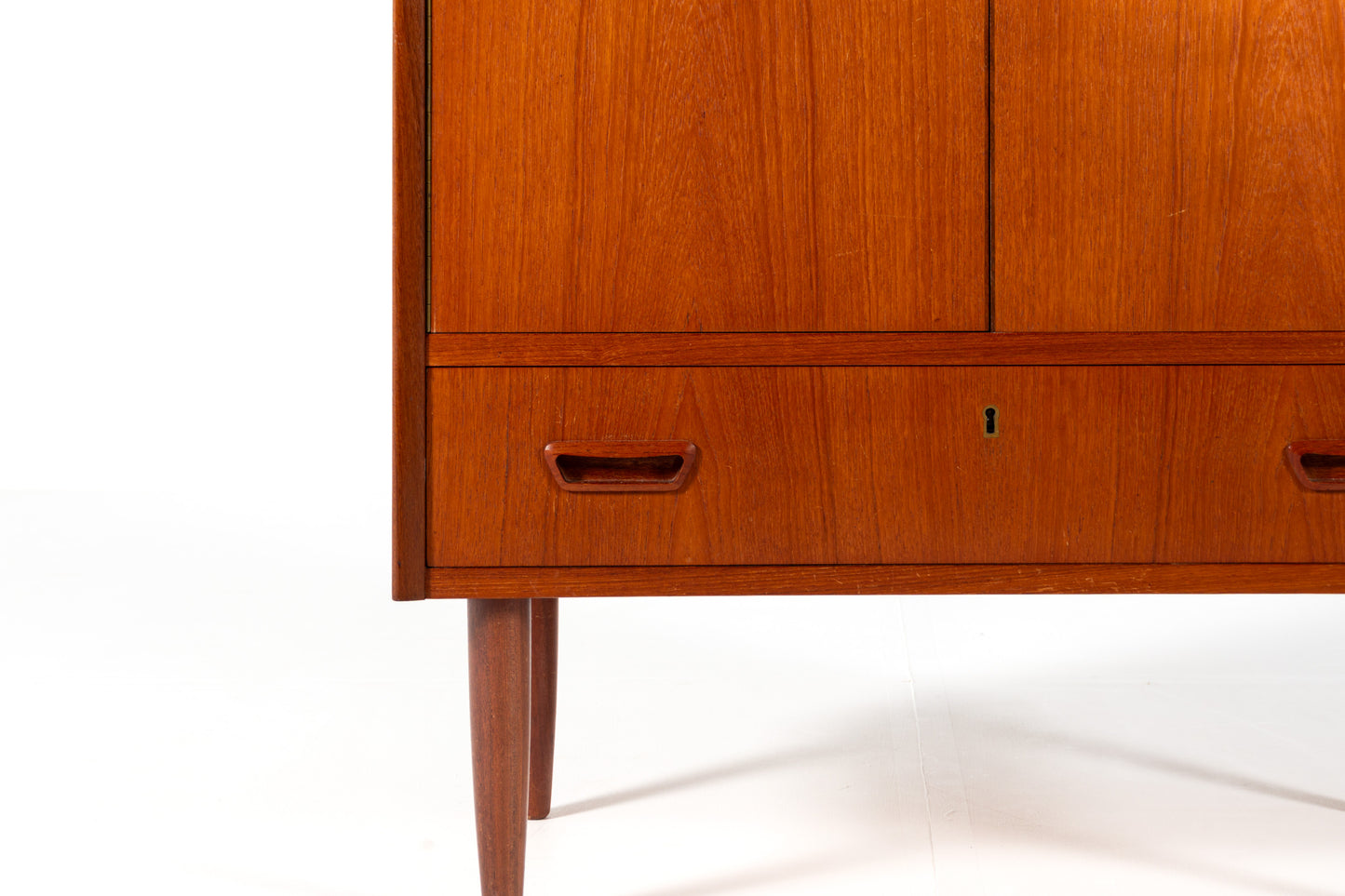 A mid-century modern wooden cabinet with a warm reddish-brown finish, featuring two upper doors and a lower drawer
