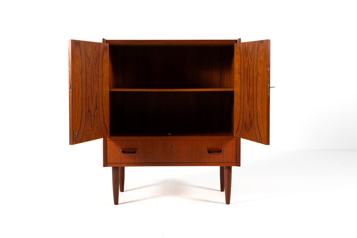 A mid-century modern wooden cabinet with a warm reddish-brown finish, featuring two upper doors and a lower drawer, with doors open