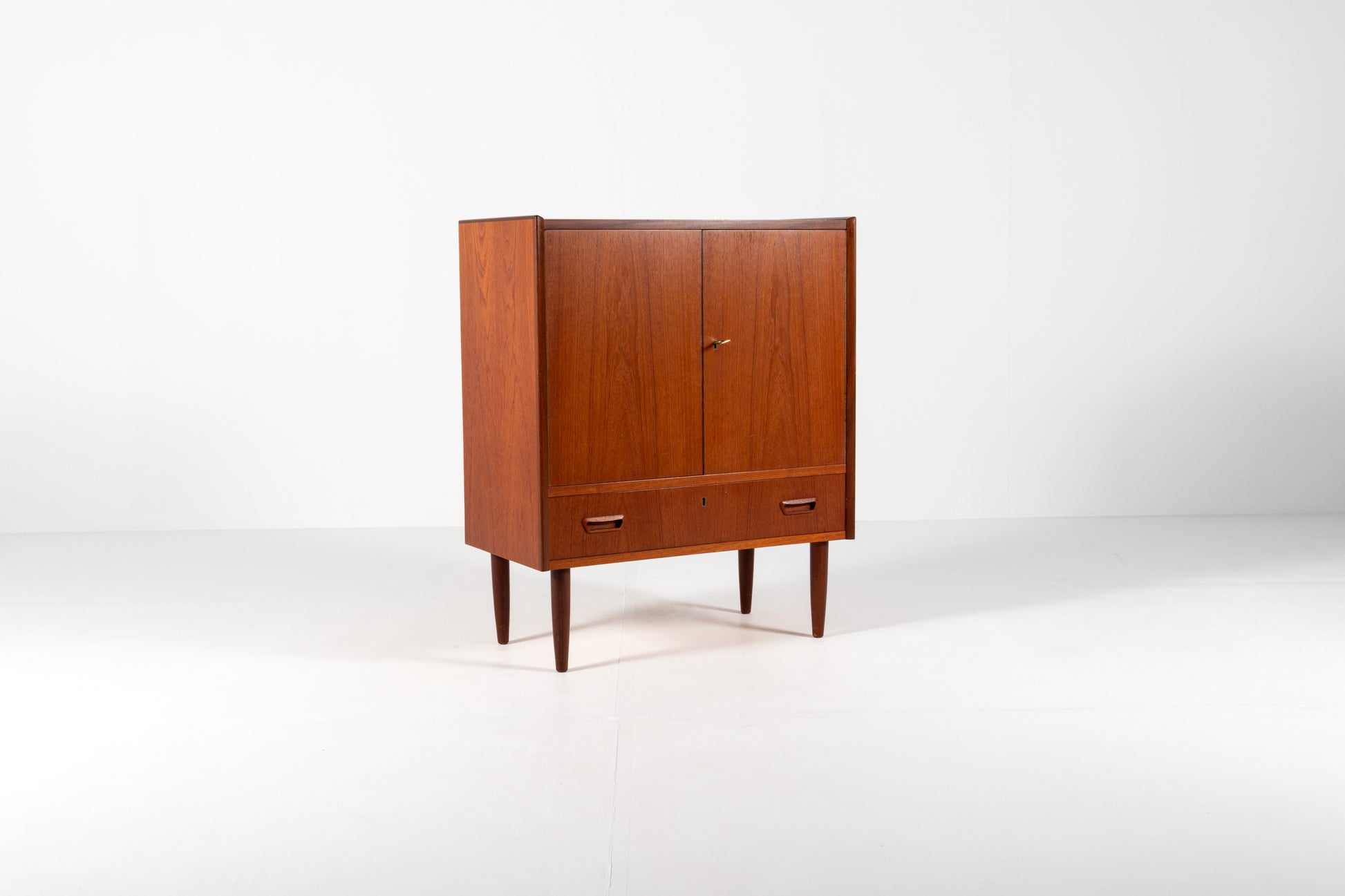 A mid-century modern wooden cabinet with a warm reddish-brown finish, featuring two upper doors and a lower drawer