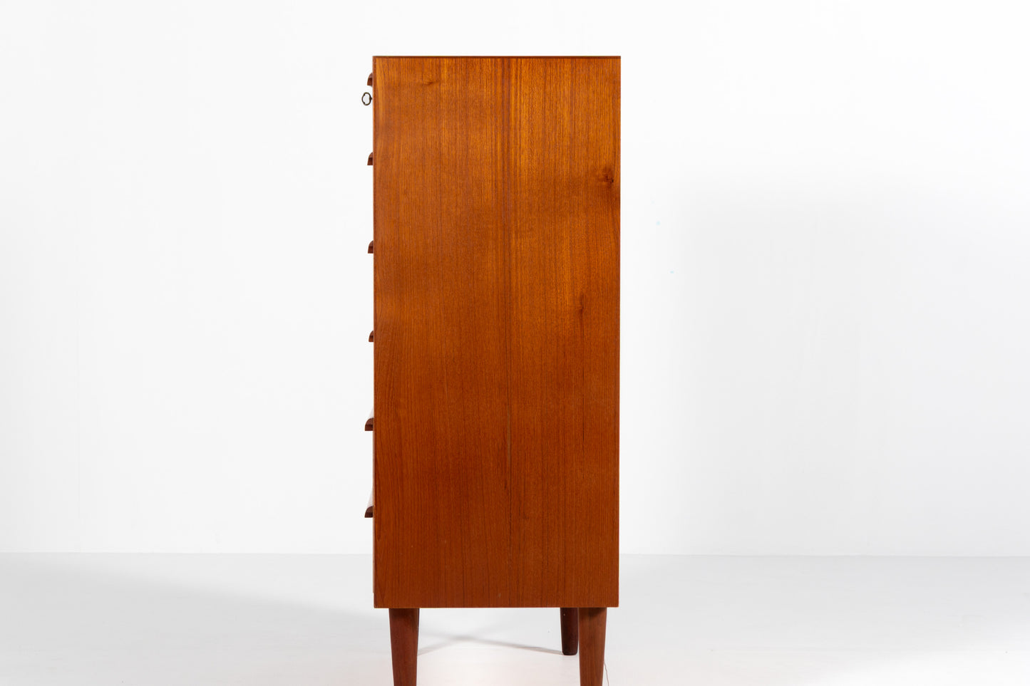 A mid-century modern wooden chest of drawers with a warm reddish-brown teak finish, side view