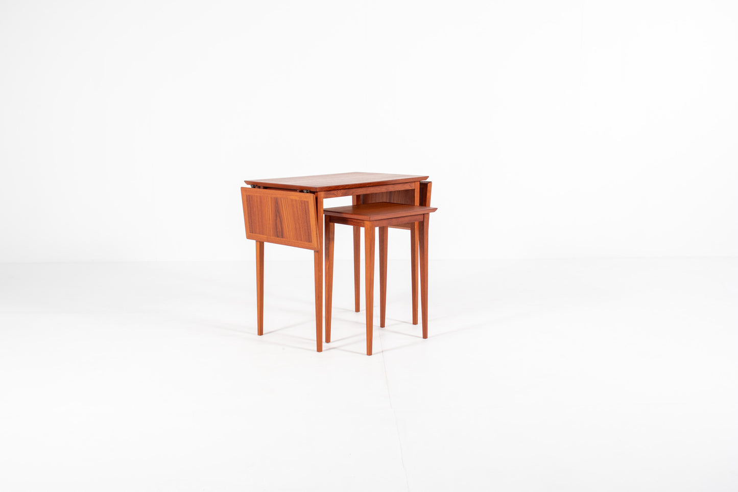 Two vintage Scandinavian teak nesting tables neatly stored together beneath the main table, showcasing the practical nesting feature.