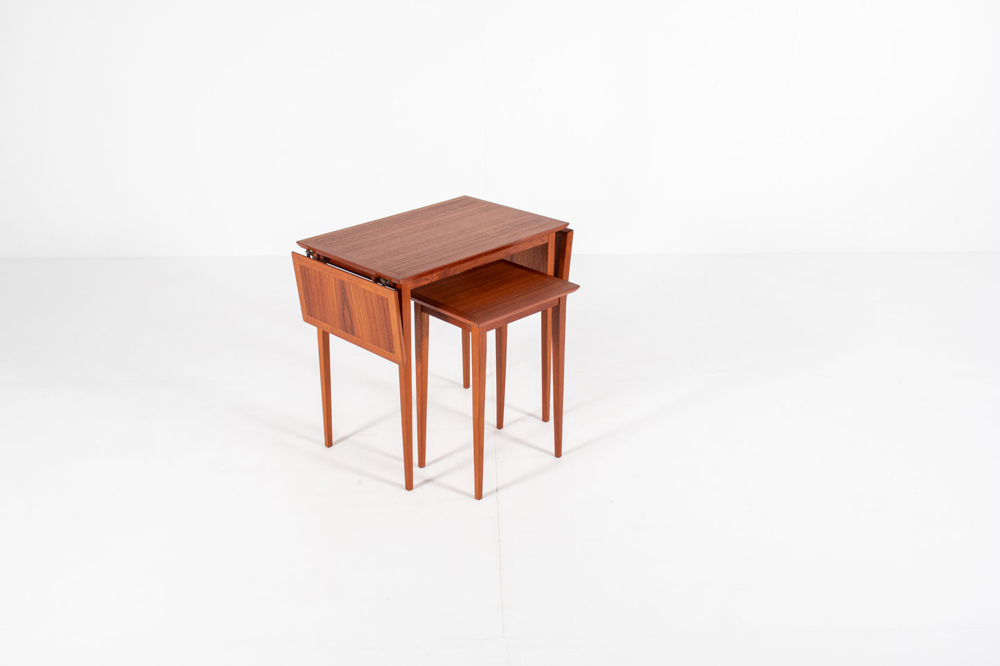 Vintage Danish nesting table set in teak with fold-out drop leaves, photographed from a three-quarter front angle showing the extendable design.