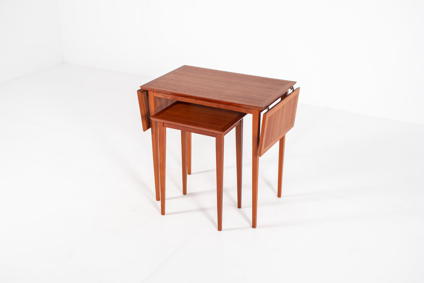 Vintage Danish nesting table set in teak with fold-out drop leaves, photographed from a three-quarter front angle showing the extendable design.
