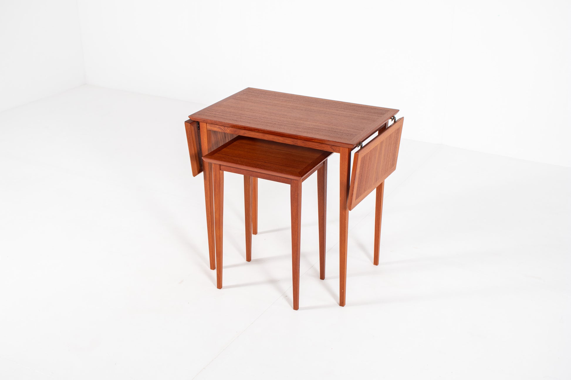 Vintage Danish nesting table set in teak with fold-out drop leaves, photographed from a three-quarter front angle showing the extendable design.