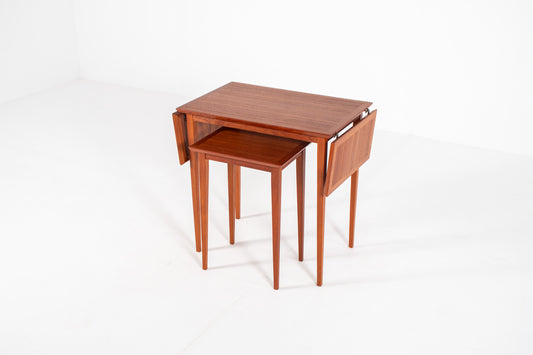 Vintage Danish nesting table set in teak with fold-out drop leaves, photographed from a three-quarter front angle showing the extendable design.