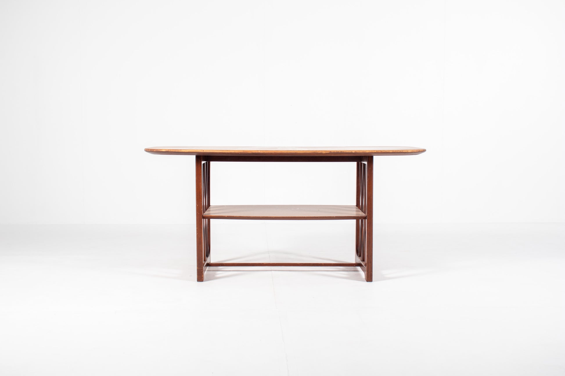 A mid-century modern wooden table designed by A.A. Patijn for Zijlstra Joure with a warm brown finish, featuring a rounded rectangular top, two open shelves, and geometric cross-brace leg supports, set against a plain white studio background.