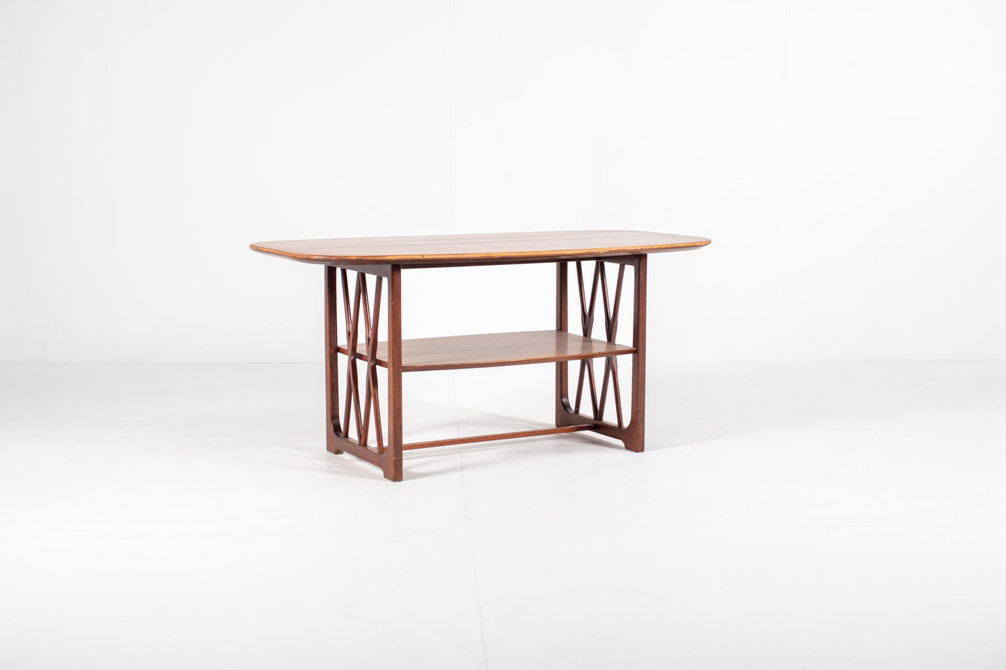 A mid-century modern wooden table designed by A.A. Patijn for Zijlstra Joure with a warm brown finish, featuring a rounded rectangular top, two open shelves, and geometric cross-brace leg supports, set against a plain white studio background.