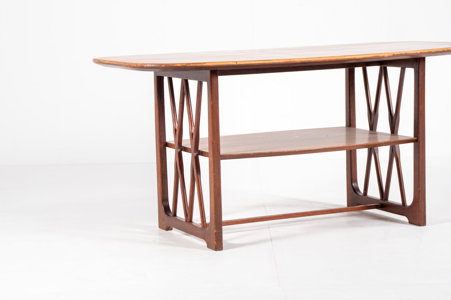A mid-century modern wooden table designed by A.A. Patijn for Zijlstra Joure with a warm brown finish, featuring a rounded rectangular top, two open shelves, and geometric cross-brace leg supports, set against a plain white studio background.