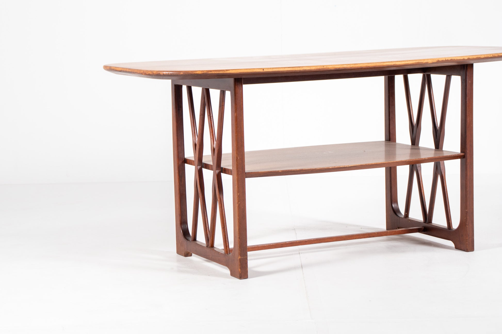 A mid-century modern wooden table designed by A.A. Patijn for Zijlstra Joure with a warm brown finish, featuring a rounded rectangular top, two open shelves, and geometric cross-brace leg supports, set against a plain white studio background.