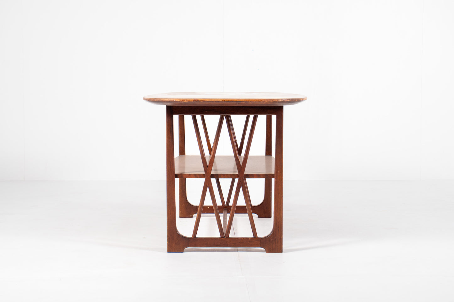 A mid-century modern wooden table designed by A.A. Patijn for Zijlstra Joure with a warm brown finish, featuring a rounded rectangular top, two open shelves, and geometric cross-brace leg supports, set against a plain white studio background, side view