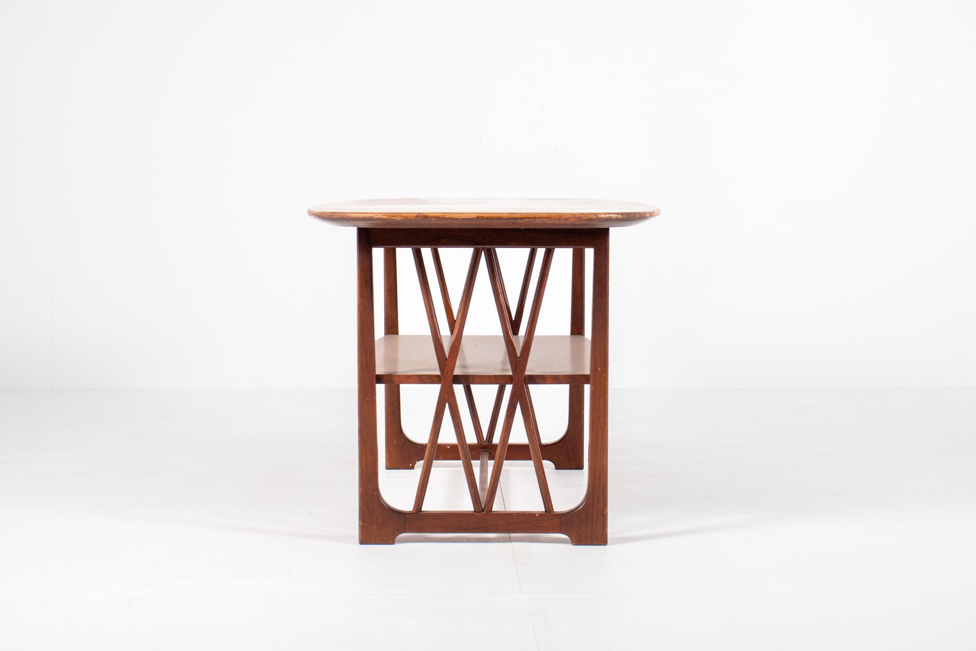 A mid-century modern wooden table designed by A.A. Patijn for Zijlstra Joure with a warm brown finish, featuring a rounded rectangular top, two open shelves, and geometric cross-brace leg supports, set against a plain white studio background, side view
