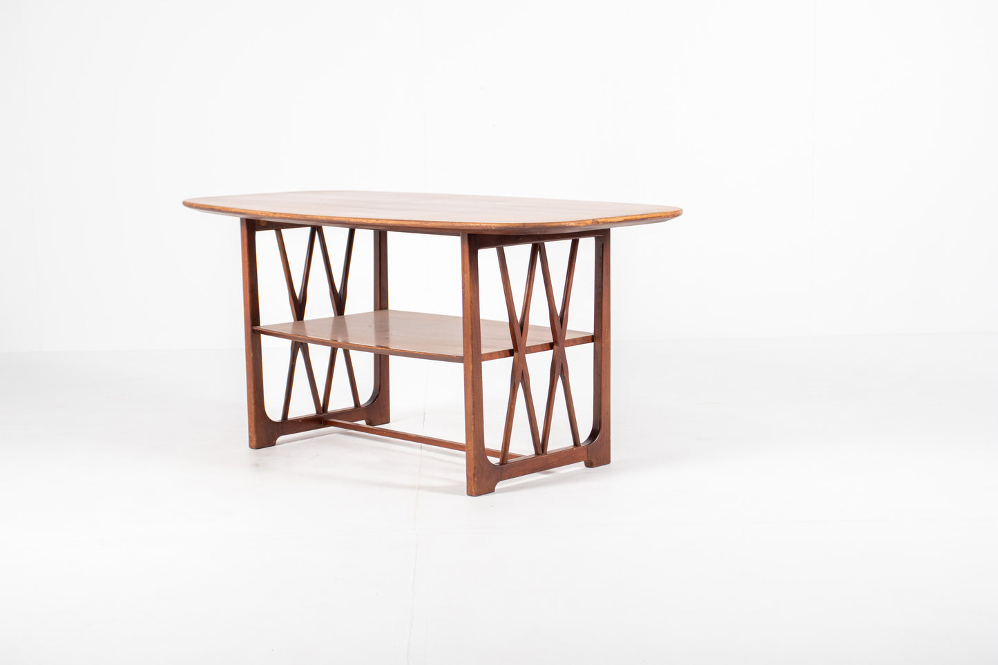 A mid-century modern wooden table designed by A.A. Patijn for Zijlstra Joure with a warm brown finish, featuring a rounded rectangular top, two open shelves, and geometric cross-brace leg supports, set against a plain white studio background.