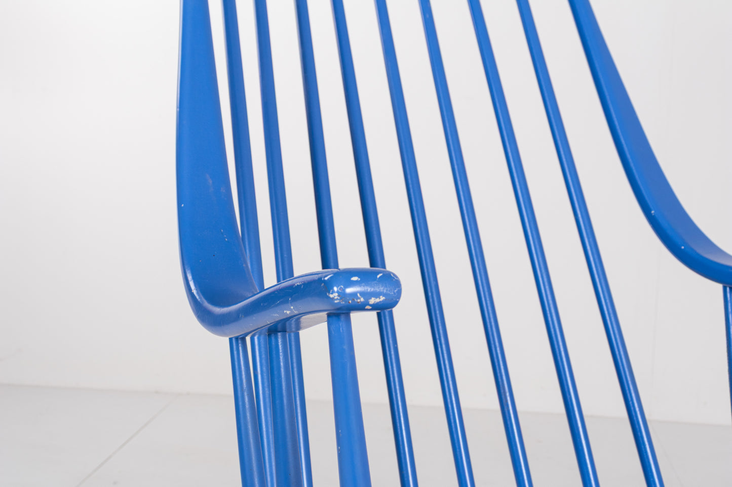 Close-up of the sculptural curved wooden armrest and spindle supports on a 1960s Scandinavian rocking chair.