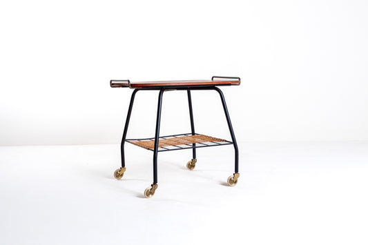 A mid-century modern bar cart with a dark wood top, black metal frame, a slatted wooden lower shelf, and brass caster wheels, photographed on a seamless white studio background.