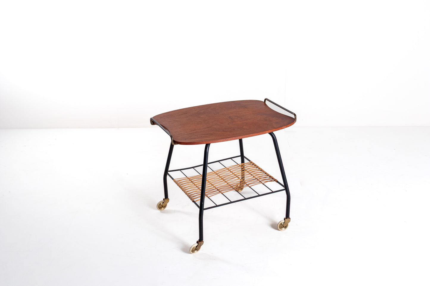 A mid-century modern serving cart with a curved reddish-brown wooden top, black metal frame, and a woven natural-fiber lower shelf on casters, photographed against a plain white studio background.