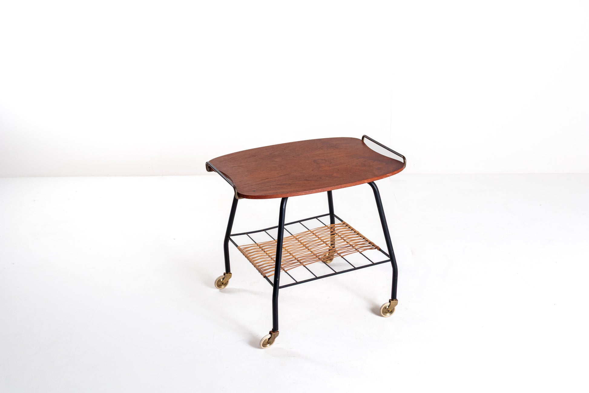 A mid-century modern serving cart with a curved reddish-brown wooden top, black metal frame, and a woven natural-fiber lower shelf on casters, photographed against a plain white studio background.