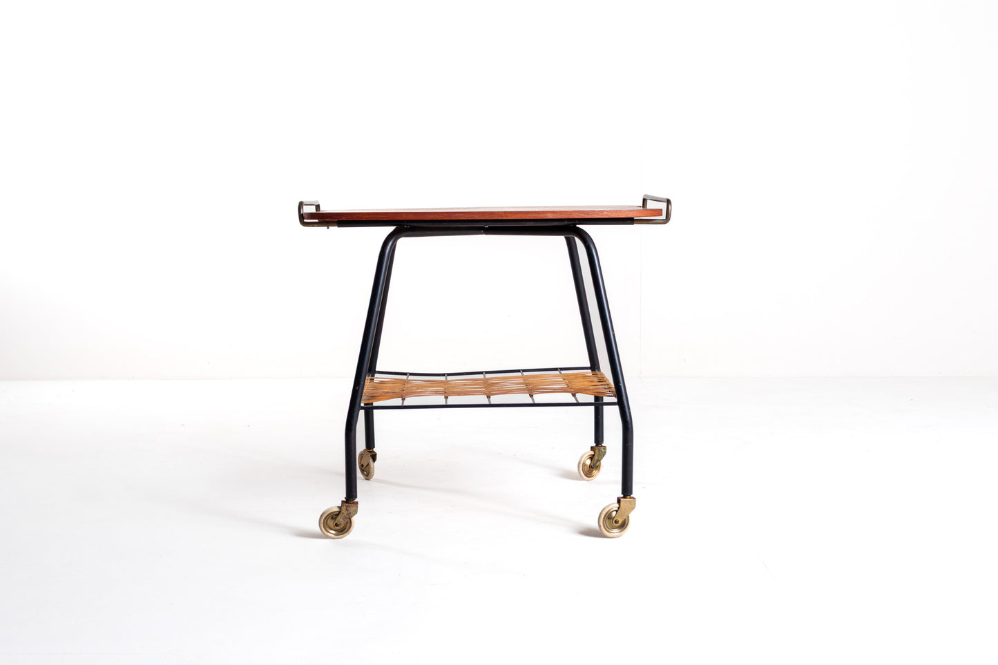 A mid-century modern rolling bar cart with a dark wood top, black metal frame, and brass caster wheels, photographed against a seamless white studio background.