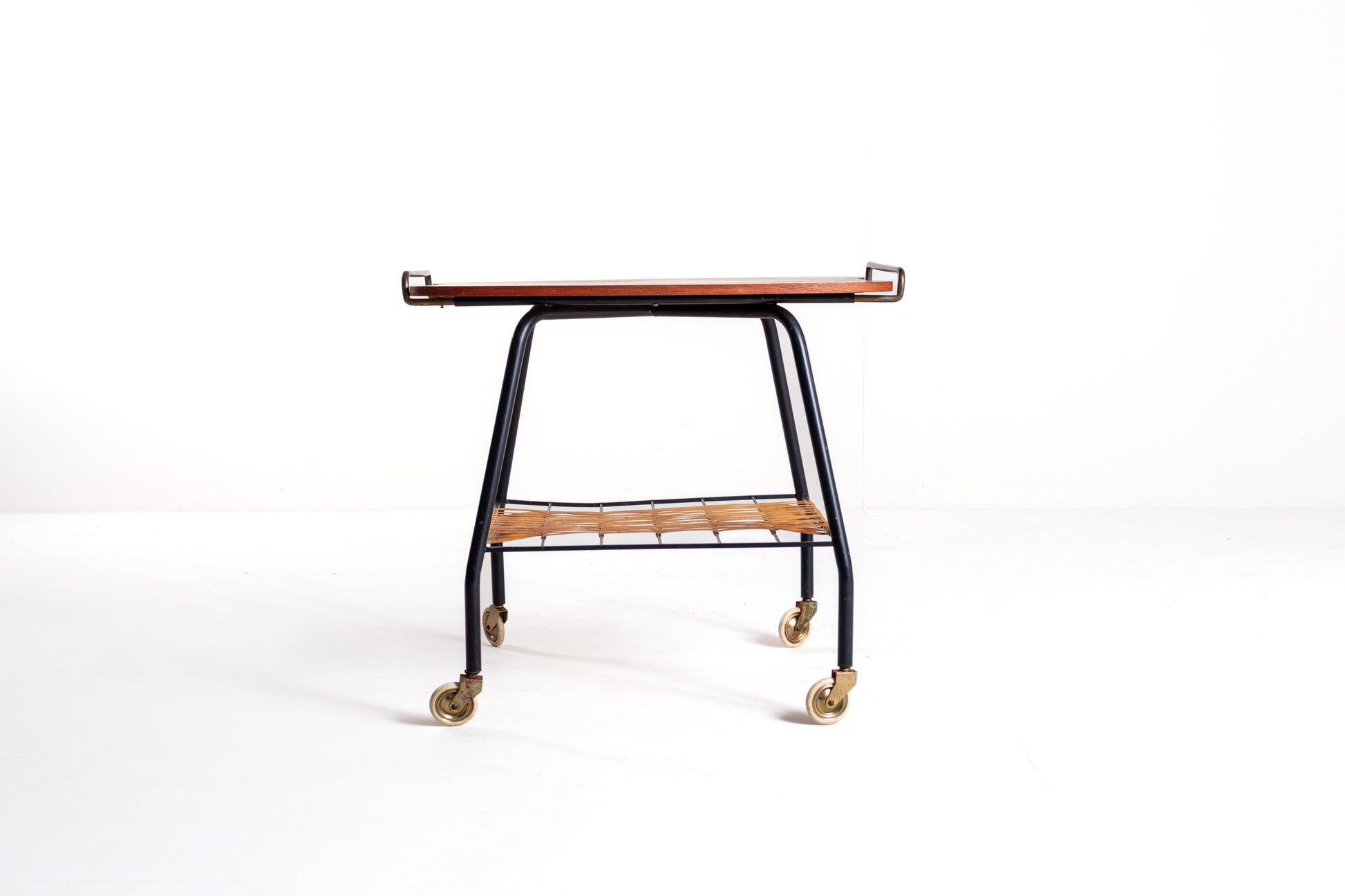 A mid-century modern rolling bar cart with a dark wood top, black metal frame, and brass caster wheels, photographed against a seamless white studio background.